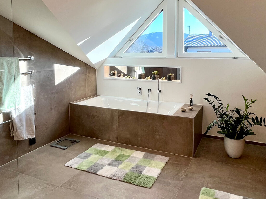 Nachher: dasselbe Bad hell und modern, mit eingefliester Badewanne ohne Stufe, bodengleicher Glasdusche und großen Fliesen in Betonoptik.