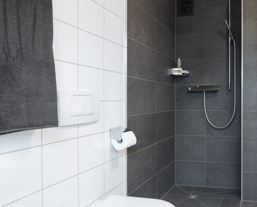 Neue bodengleiche Dusche in Dornbirn mit anthrazitfarbenen Fliesen in Schieferoptik, eingefügt zwischen bestehendem WC und Holztür.