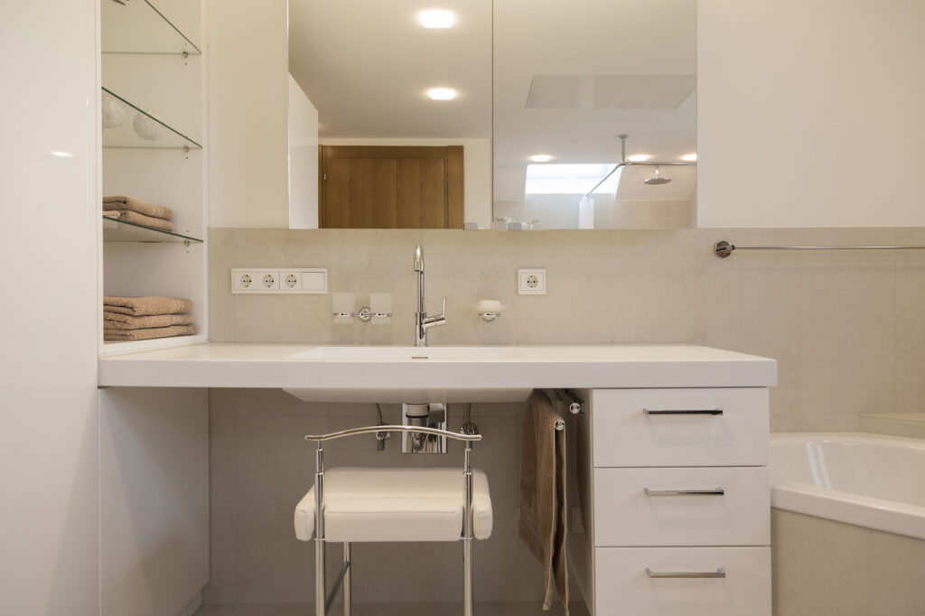Frontalansicht des unterfahrbaren Waschtischs mit Sitzhocker, Schubladenelement, offenem Regal und Spiegelschrank.
