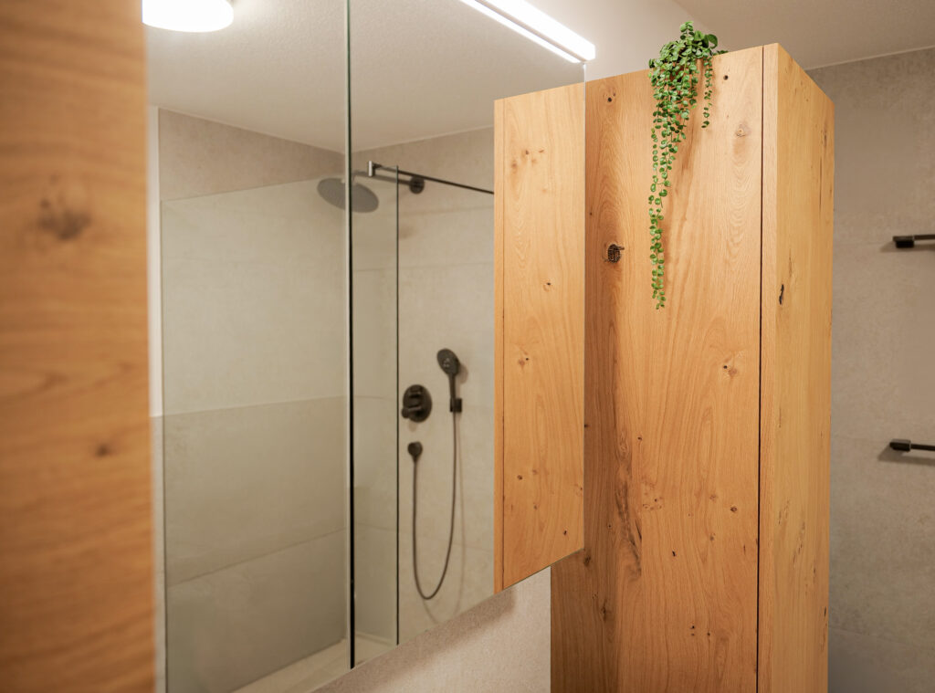 Nahaufnahme des Hochschranks aus Asteiche mit Hängepflanze, im Spiegelschrank spiegelt sich die Dusche.
