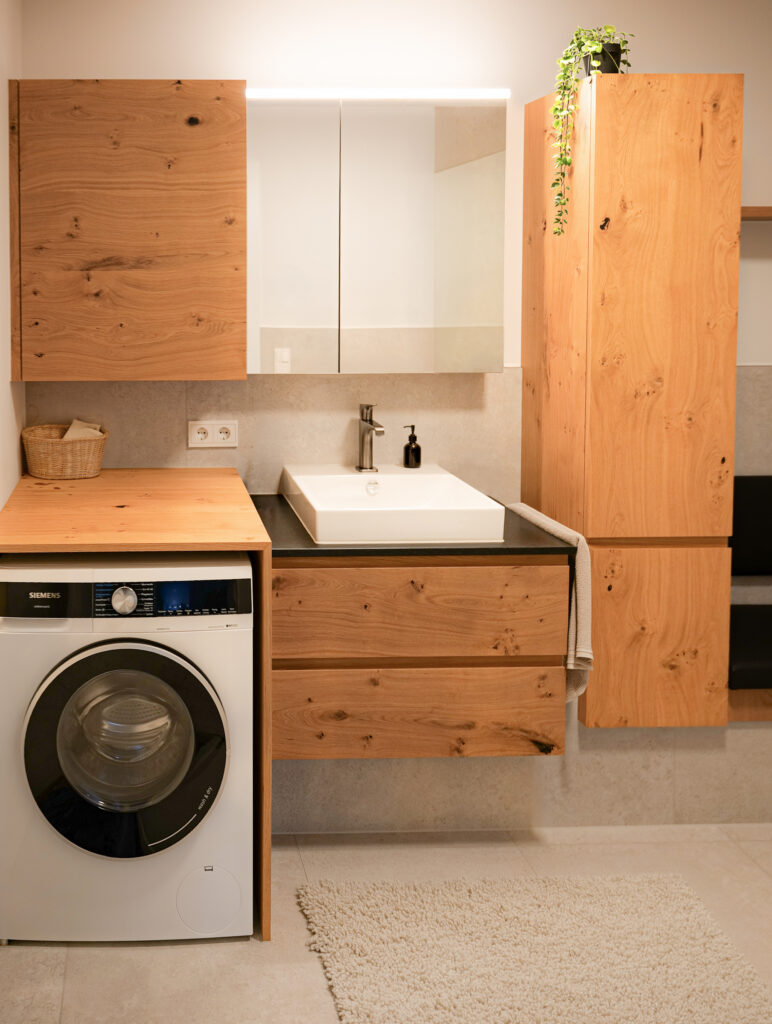 Waschplatz mit Aufsatzbecken auf Eichen-Unterschrank, beleuchtetem Spiegelschrank und integrierter Waschmaschine unter einer Holzablage.