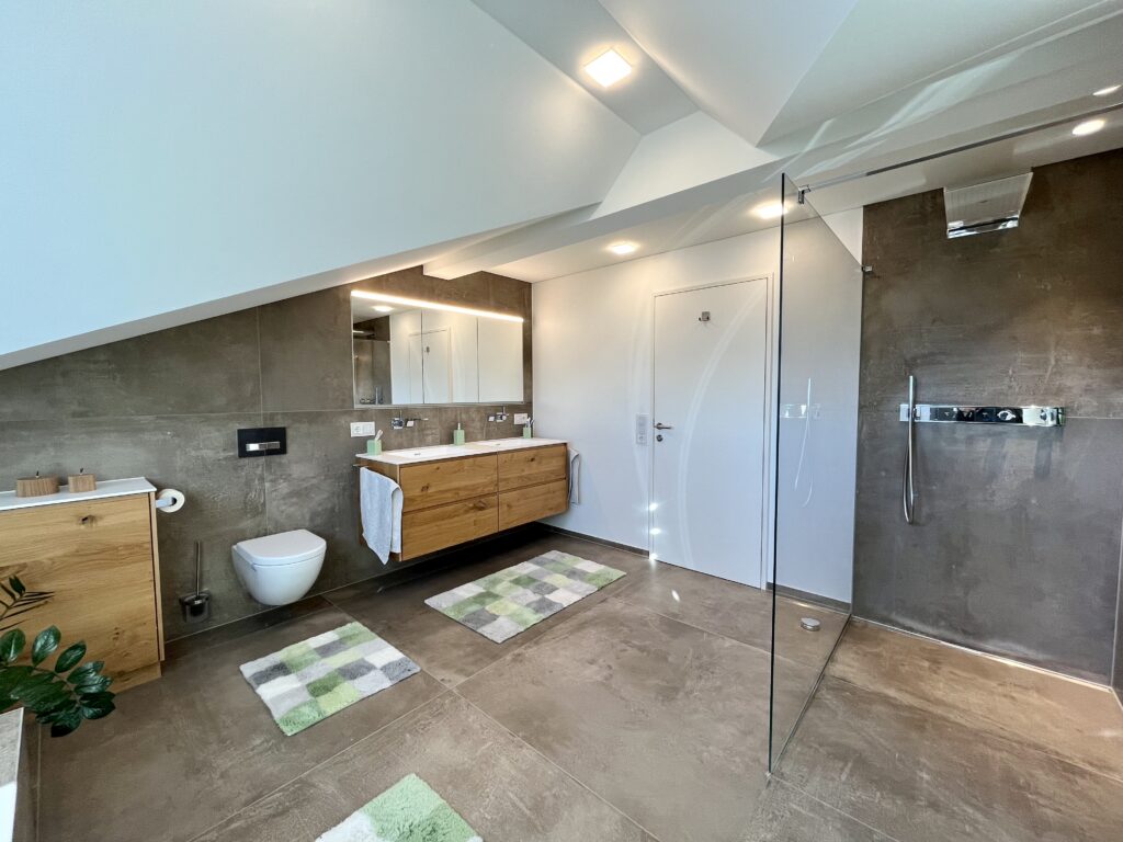 Großzügiges Dachgeschoss-Bad in Meiningen mit Doppelwaschtisch aus Eiche, Hänge-WC und bodengleicher Dusche mit Glaswand und Wandthermostat.