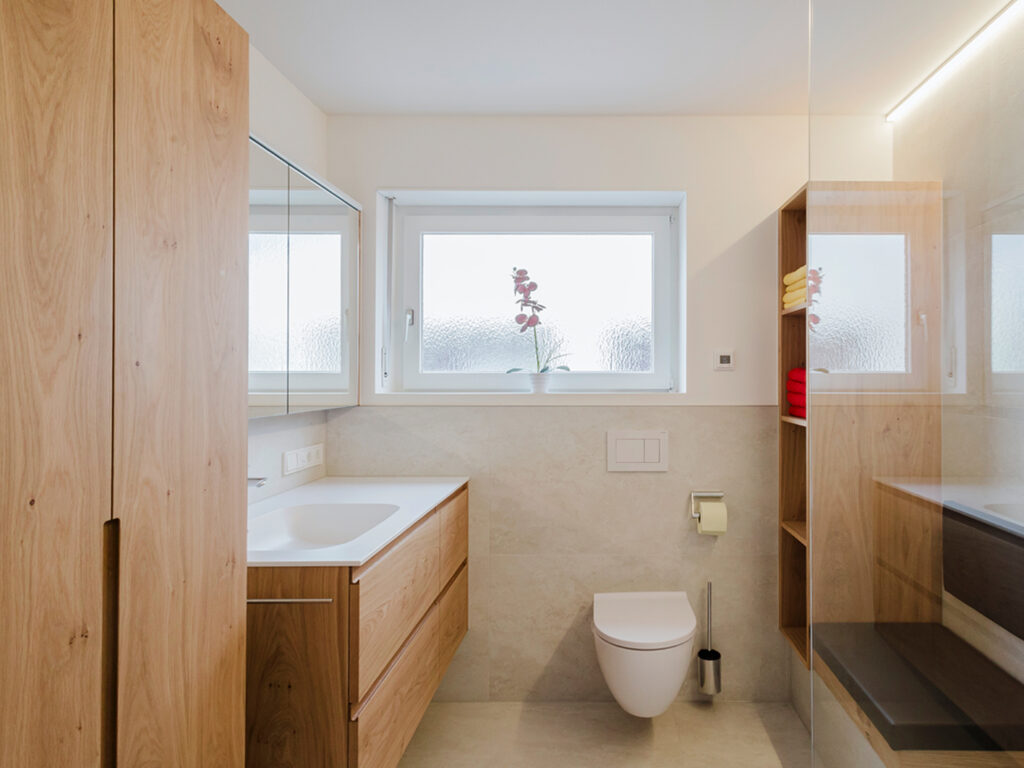 Nachher: dasselbe Bad hell und offen, mit Eichenmöbeln, Hänge-WC, Sitzbank und Dusche statt Badewanne.