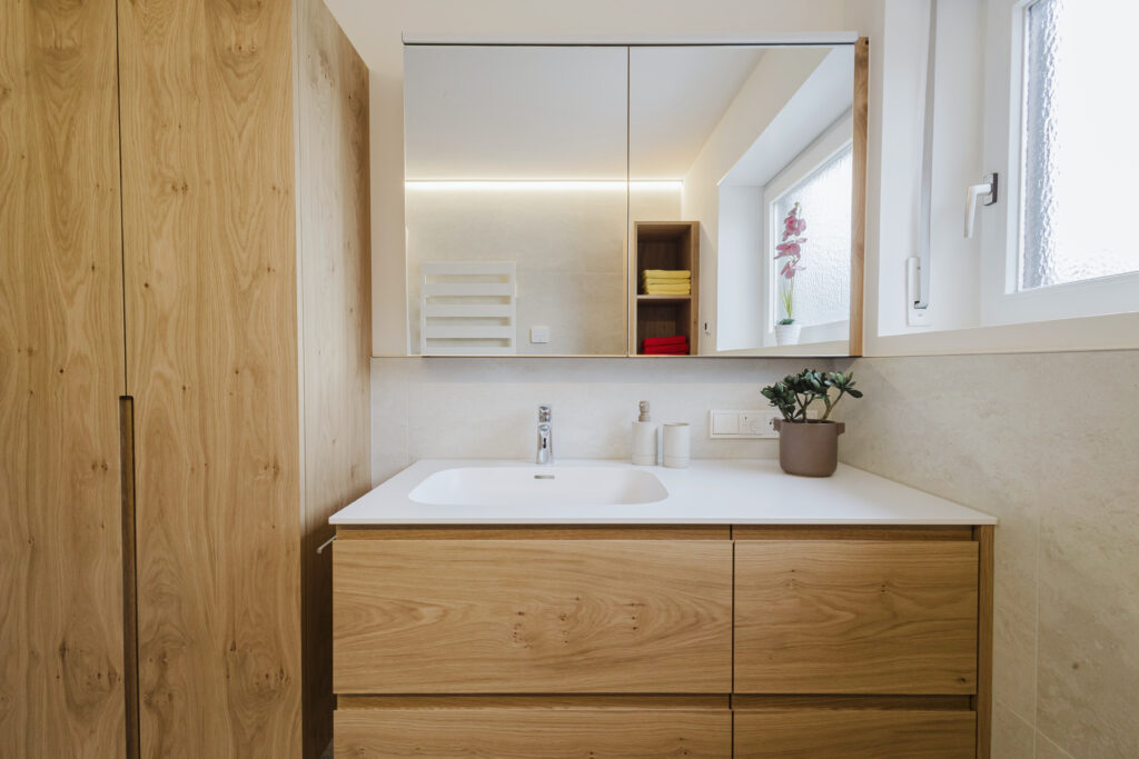 Frontalansicht des Waschtischs mit Eichenschubladen, Spiegelschrank und hohem Eichenschrank mit Griffleiste.