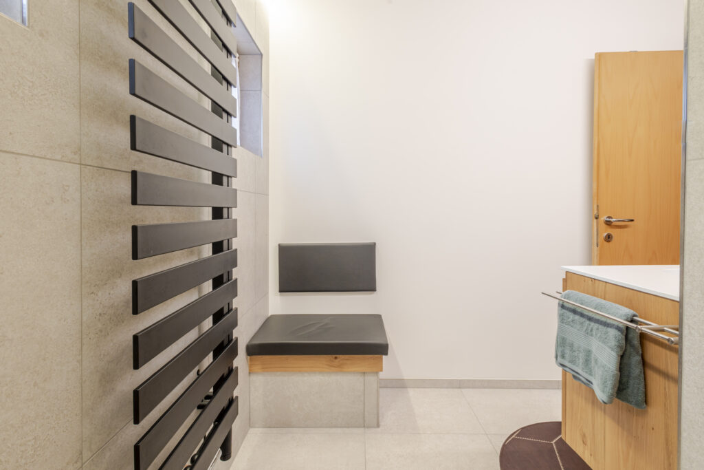 Gepolsterte Sitzbank mit Rückenlehne zwischen schwarzem Designheizkörper und Waschtisch aus Eiche.